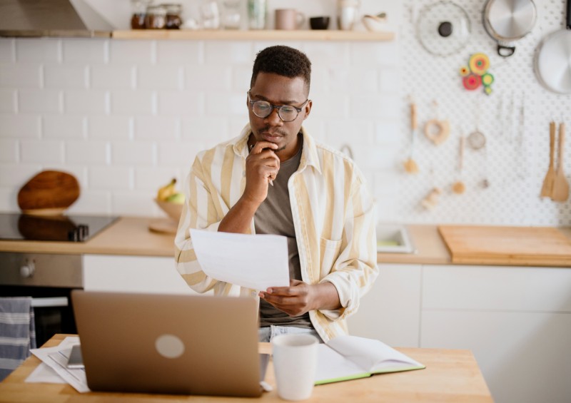 A man looking on his laptop and looking at documents