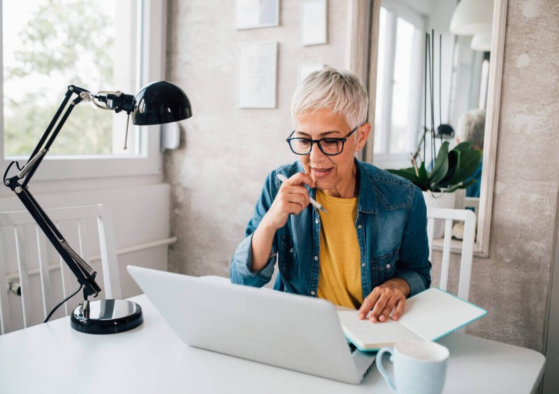 A mature lady sat at her desk looking at her laptop