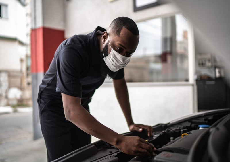 A mechanic servicing a car with a face mask on