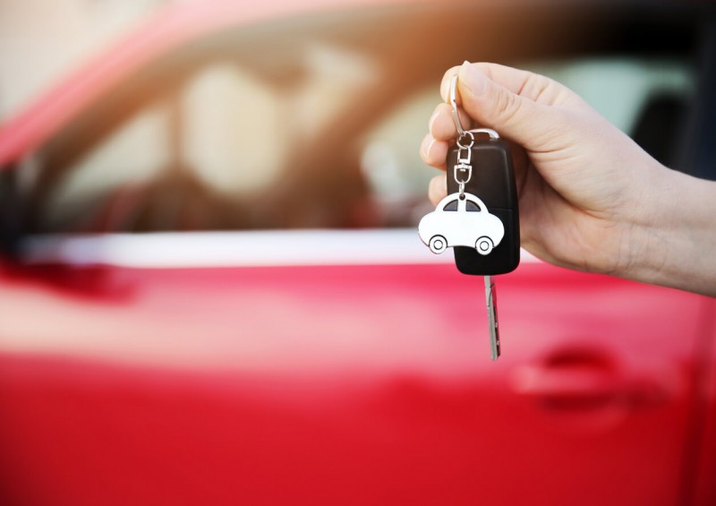 A new red car behind a person holding car keys