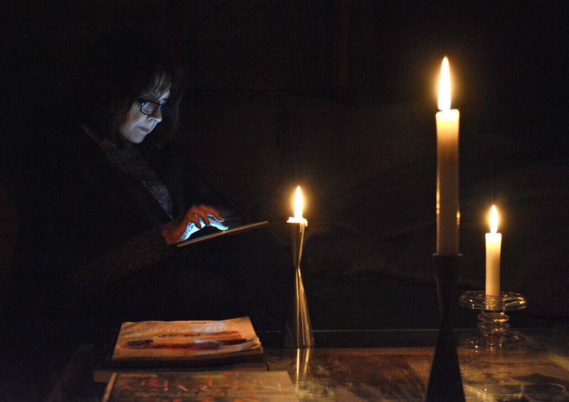 A woman at home on her ipad in the dark with candles lit