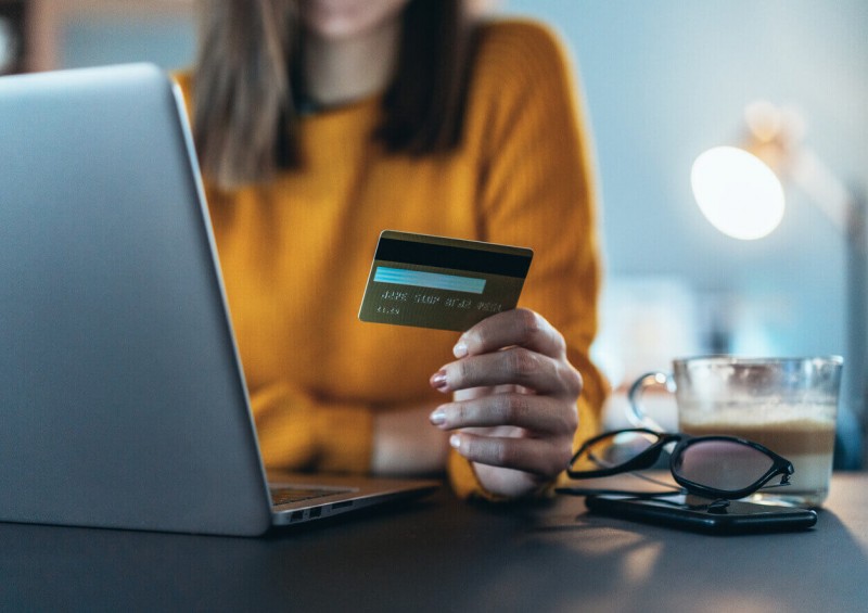 A woman looking at her credit card while on the laptop