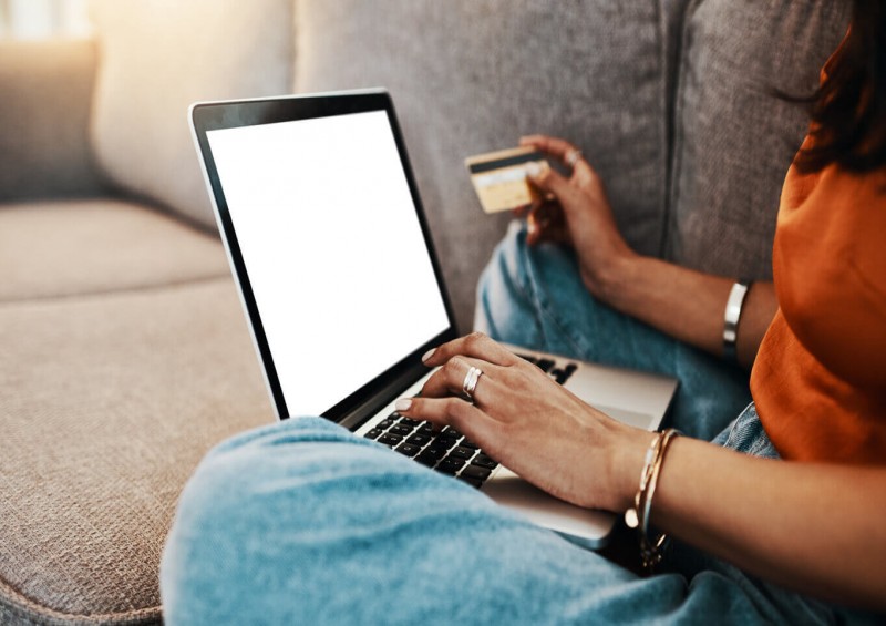 A woman looking on her laptop while holding her bank card