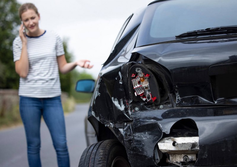 A woman on the phone next to her damaged car
