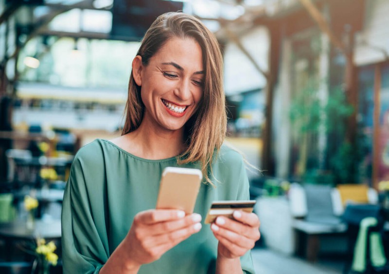 A woman smiling at her phone and holding a credit card