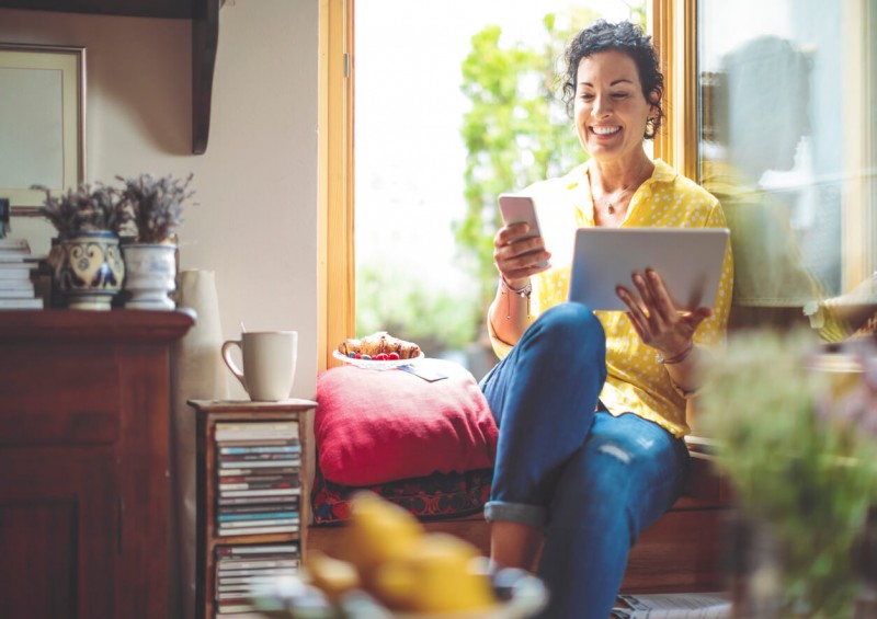 A woman smiling looking at her phone and tablet