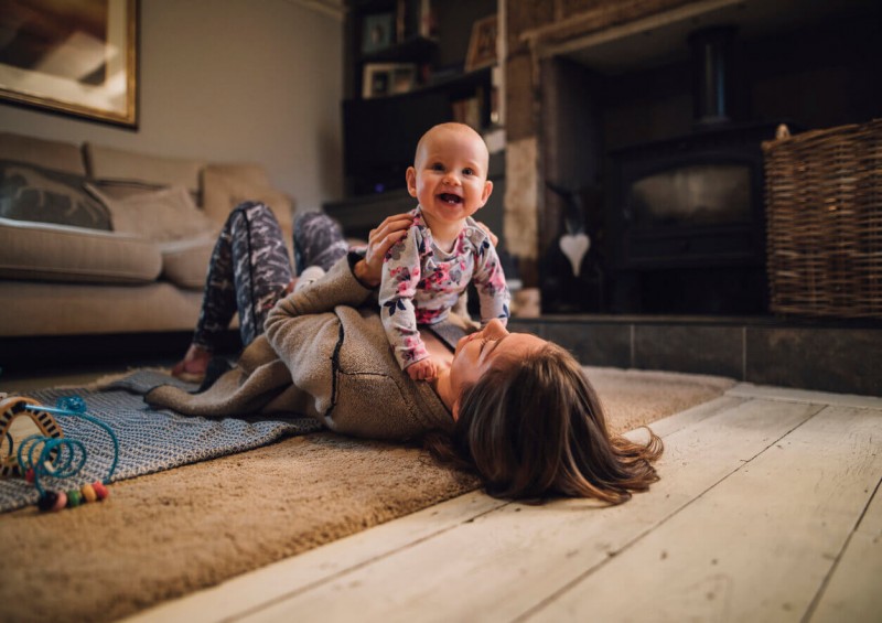 Mother on the living room floor laughing with her baby