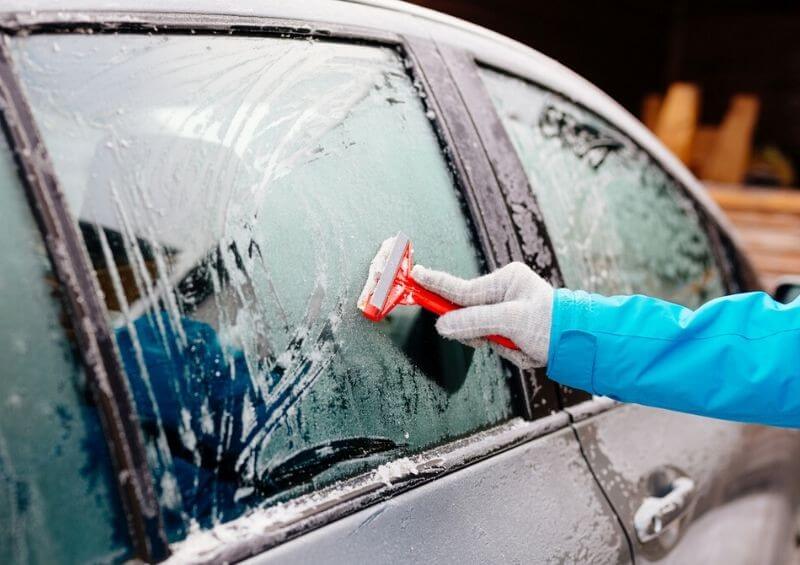 Person de icing their car with an ice scraper during winter