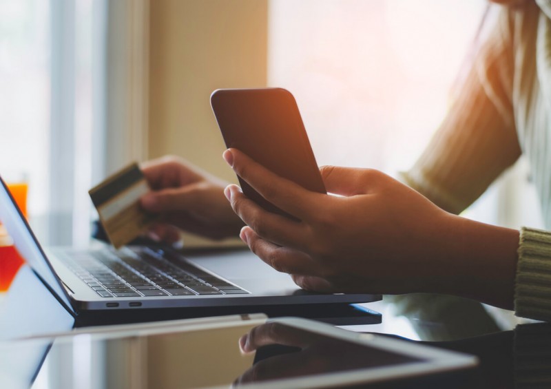 Someone on their laptop holding a bank card and mobile phone
