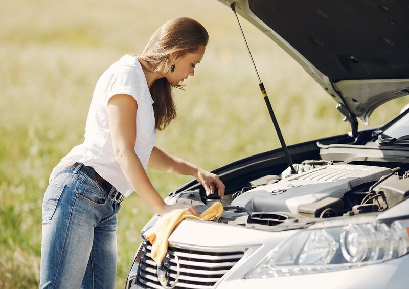 Woman looking at engine with car bonnet up after breaking down