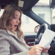 A female driver inside car looking shocked at a document