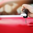 A new red car behind a person holding car keys